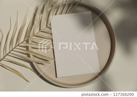 Empty greeting card, invitation mockup, envelope, plate in sunlight. Beige table background. Dry palm leaf. Long shadows. Elegant summer wedding, birthday template, web banner. Flat lay, top view. Empty greeting card, invitation mockup, envelope, plate in sunlight. Beige table background. Dry palm leaf. Long shadows. Elegant summer wedding, birthday template, web banner. Flat lay, top view. 127168200