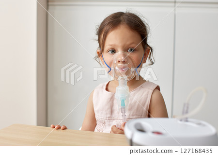 cute little toddler girl inhaling medicine on nebulizer and holding it on her own 127168435