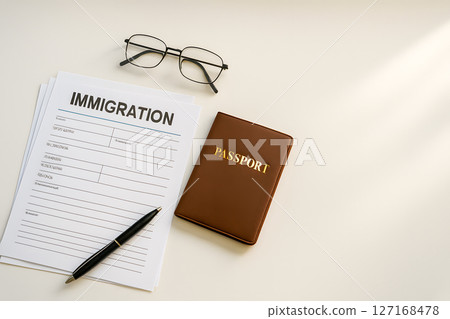 Immigration form, passport, pen, and glasses on desk, signifying global travel, visa application, and legal residency procedures, with copy space 127168478