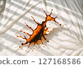 A dynamic brown liquid violently splashes across crisp white crumpled fabric, clearly illustrating a common household cleaning challenge, unexpected mess, or laundry dilemma 127168586