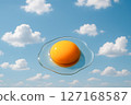 Abstract stylized fried egg yolk floating against a clear blue sky with fluffy white clouds, representing a fresh start and lightness with ample copy space 127168587