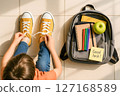 Overhead view of a young child tying vibrant yellow shoelaces beside a school backpack filled with supplies and a Good luck note 127168589