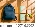 Organized blue backpack with school supplies, including notebooks, pencils, and a healthy lunchbox on wooden floor, symbolizing back to school readiness 127168592