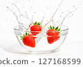 Three fresh red strawberries splash into a glass bowl of clear water, signifying natural freshness, healthy eating, and purity with ample copy space 127168599