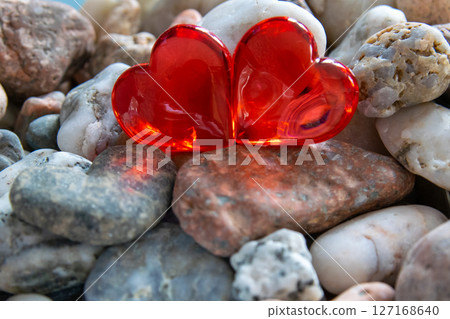 Two glass red bright heart on other stones near the river with sun weather. Two glass red bright heart on other stones near the river with sun weather. 127168640