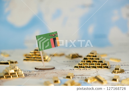 A miniature Zambian flag stands among golden bars on a world map, symbolizing national wealth, resource extraction, and global economic investment with open copy space 127168726