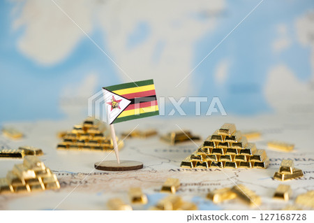Miniature Zimbabwe flag stands amidst numerous precious shiny gold bars on a blurred world map, representing the nation's economic wealth and financial potential 127168728