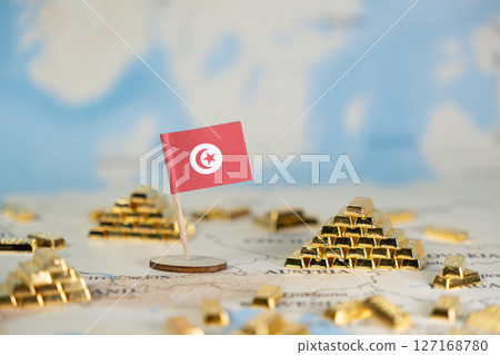 Tunisian national flag stands proudly amidst miniature gold bars on a world map, representing national economic stability, wealth, and global investment 127168780
