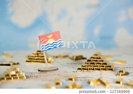 Miniature Kiribati national flag standing on a blurred global map with many glistening golden bar stacks, symbolizing island nation wealth, economic potential, and financial stability 127168806