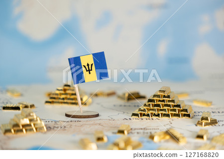 Miniature Barbados flag standing alongside piles of shiny gold bars on a blurred world map, symbolizing national wealth, economic stability, and global investment 127168820