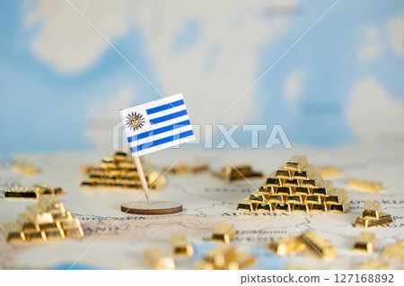Miniature Uruguay flag stands proudly surrounded by golden bars on a global map, signifying national economic power, trade, and wealth accumulation, featuring ample copy space 127168892