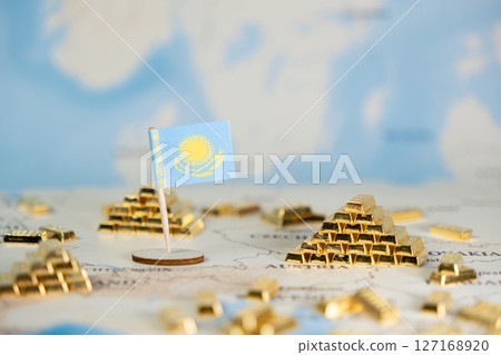 Miniature flag of Kazakhstan stands among gold bars on a world map, representing national economic wealth, gold reserves, and international finance with copy space 127168920