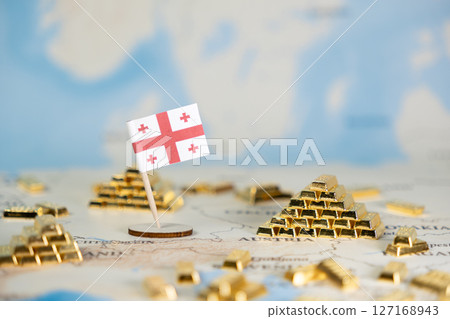 Georgian flag standing alongside gold bars on a world map, representing national economic power, global wealth, and financial investment with copy space 127168943