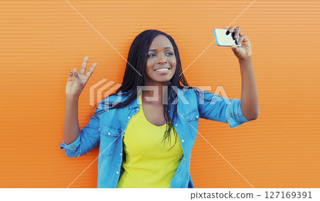 Happy African young woman laughs taking selfie with phone, cheerful black girl smiles on smartphone Happy African young woman laughs taking selfie with phone, cheerful black girl smiles on smartphone 127169391