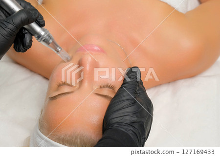 Microneedle RF lifting procedure. A cosmetologist performs a facial rejuvenation procedure on a woman. Hardware cosmetology. 127169433