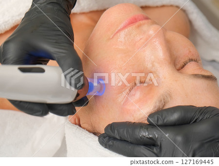 Close-up portrait of a beautiful aged woman during microneedling with dermapen from a beautician. 127169445