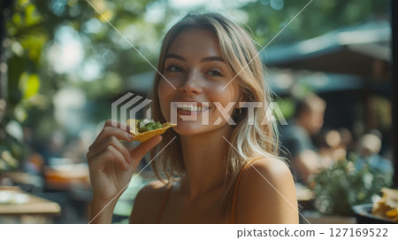 Cheerful Woman Snacking on Nachos at a Sunny Patio 127169522
