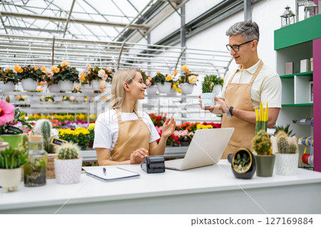 A Caucasian man and woman are in a flower shop, interacting with each other while looking at a small plant. 127169884