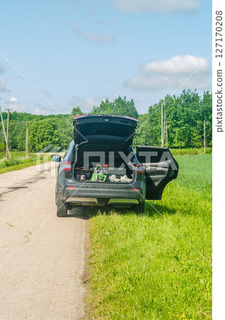 Open trunk of SUV car parked on rural road by green fields on sunny day. High quality photo 127170208