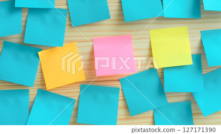 A centered pink sticky note stands out amidst a variety of colorful notes. primarily blue, yellow, and orange arranged on a light wooden surface A centered pink sticky note stands out amidst a variety of colorful notes. primarily blue, yellow, and orange arranged on a light wooden surface 127171390