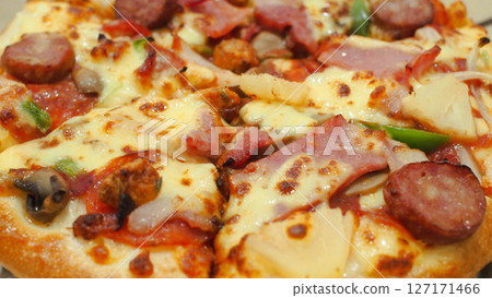 Close-up of a supreme pizza loaded with cheese, sausage, ham, pepperoni, mushrooms, green bell peppers, and pineapple chunks. Close-up of a supreme pizza loaded with cheese, sausage, ham, pepperoni, mushrooms, green bell peppers, and pineapple chunks. 127171466