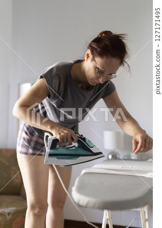 Woman ironing clothes on ironing board at home Woman ironing clothes on ironing board at home 127171495