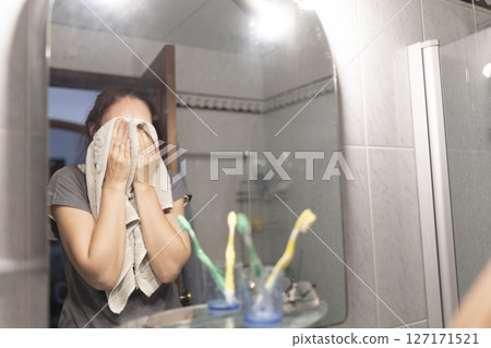 Woman drying her face with a towel in the bathroom after showering 127171521