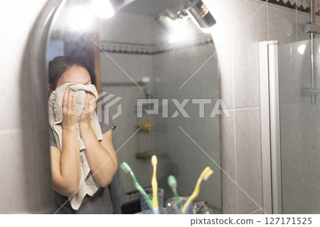 Woman drying her face with a towel after showering in the bathroom Woman drying her face with a towel after showering in the bathroom 127171525