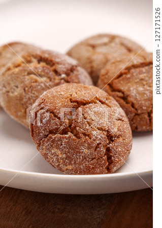 Festive ginger snap cookies in beige ceramic plate on wooden table close up Festive ginger snap cookies in beige ceramic plate on wooden table close up 127171526