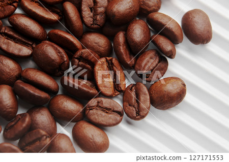 Roasted Arabica coffee beans scattered on white ribbed paper of store packaging. Macro.  127171553