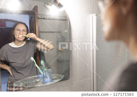 Woman brushing teeth in bathroom mirror at home 127171563