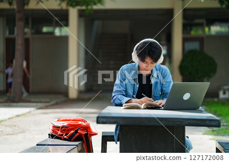 Portrait of a young Asian male college student e-learning using laptop on the bench on campus. 127172008