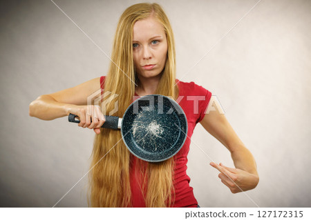 Angry girl holding scratched frying pan Angry girl holding scratched frying pan 127172315