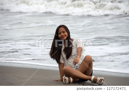 young asian woman smiling sitting on the coast of tropical wavy sea 127172471