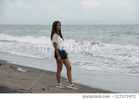 Confident woman standing on beach near sea waves 127172472