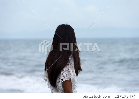 a young woman stands alone on the seashore and looks into the distance at the sea waves 127172474