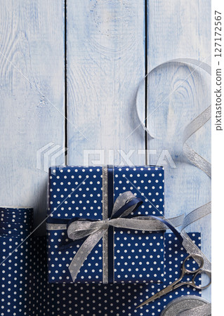 Hand-wrapped blue gift. Rolls of wrapping paper, scissors, ribbon, ready-wrapped gifts. Blue wooden background, space for your text. Hand-wrapped blue gift. Rolls of wrapping paper, scissors, ribbon, ready-wrapped gifts. Blue wooden background, space for your text. 127172567