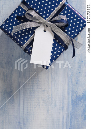 The blue gift box is tied with a silver-dark blue ribbon. An empty white tag hangs from the bow, on which you can write a message. The blue gift box is tied with a silver-dark blue ribbon. An empty white tag hangs from the bow, on which you can write a message. 127172571