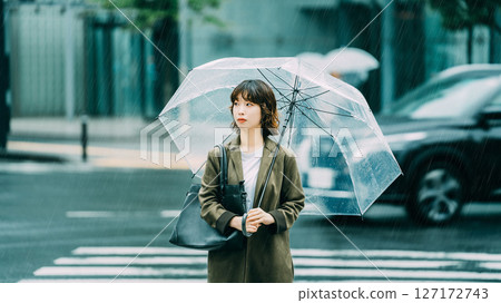 A woman walking through an intersection with an umbrella (rainy season, June) 127172743