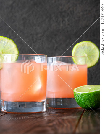 Two guava margaritas with lime wheels glow against rich dark cocktail backdrop 127173440