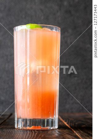 Guava Collins cocktail sparkles in tall glass with lime against dark backdrop Guava Collins cocktail sparkles in tall glass with lime against dark backdrop 127173443