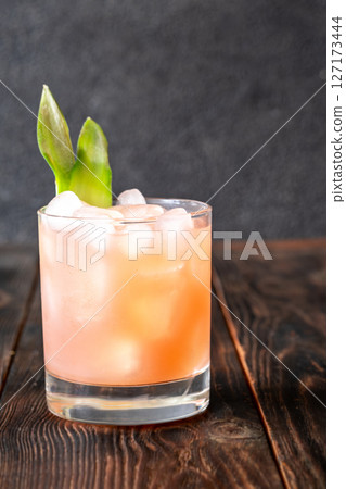 Guava rum punch cocktail with pineapple garnish on moody tropical evening backdrop Guava rum punch cocktail with pineapple garnish on moody tropical evening backdrop 127173444