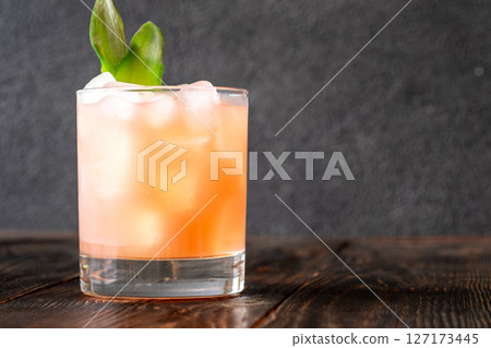 Guava rum punch cocktail with pineapple garnish on moody tropical evening backdrop Guava rum punch cocktail with pineapple garnish on moody tropical evening backdrop 127173445
