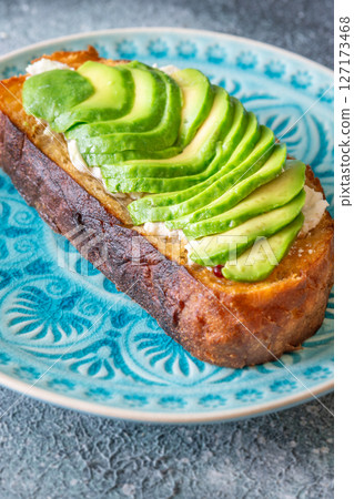 Toasted white bread with labneh spread and avocado slices on blue plate 127173468