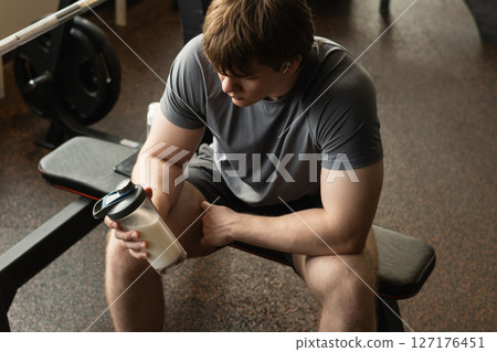Close up shot of man at gym holding protein shaker. Bodybuilder during strength training. Fitness healthy lifestyle concept. Hydration after workout session. Supplement product Close up shot of man at gym holding protein shaker. Bodybuilder during strength training. Fitness healthy lifestyle concept. Hydration after workout session. Supplement product 127176451