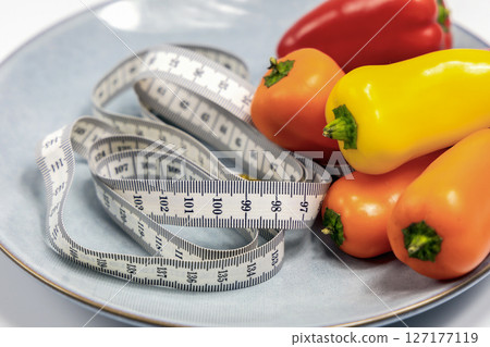 Plate with sweet peppers and a measuring tape. Concept of diet and weight loss Plate with sweet peppers and a measuring tape. Concept of diet and weight loss 127177119