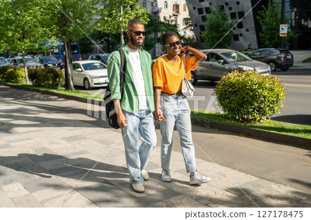Happy lovers couple of African American students walking together, holding hands, laughing merrily. Happy lovers couple of African American students walking together, holding hands, laughing merrily. 127178475