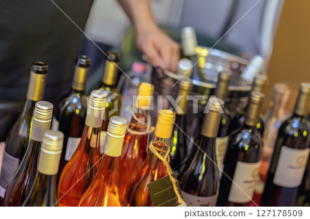 Closeup of assorted wine bottles with man sommelier in background arranging drinks on event table. Concept of wine tasting, celebration and sommelier service at festival Closeup of assorted wine bottles with man sommelier in background arranging drinks on event table. Concept of wine tasting, celebration and sommelier service at festival 127178509