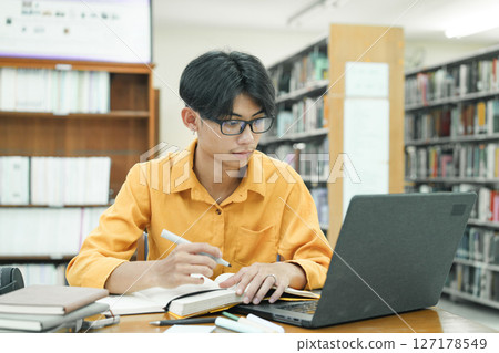 Young collage student using computer and mobile device studying online. 127178549