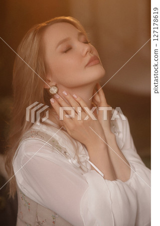 Young woman touching her neck with closed eyes in soft warm light, close-up portrait 127178619